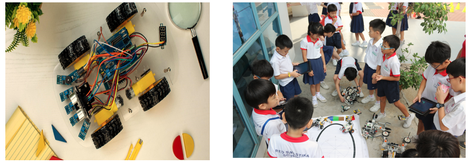 A robot car with wiring beside children in school uniforms gathered around robots outdoors.